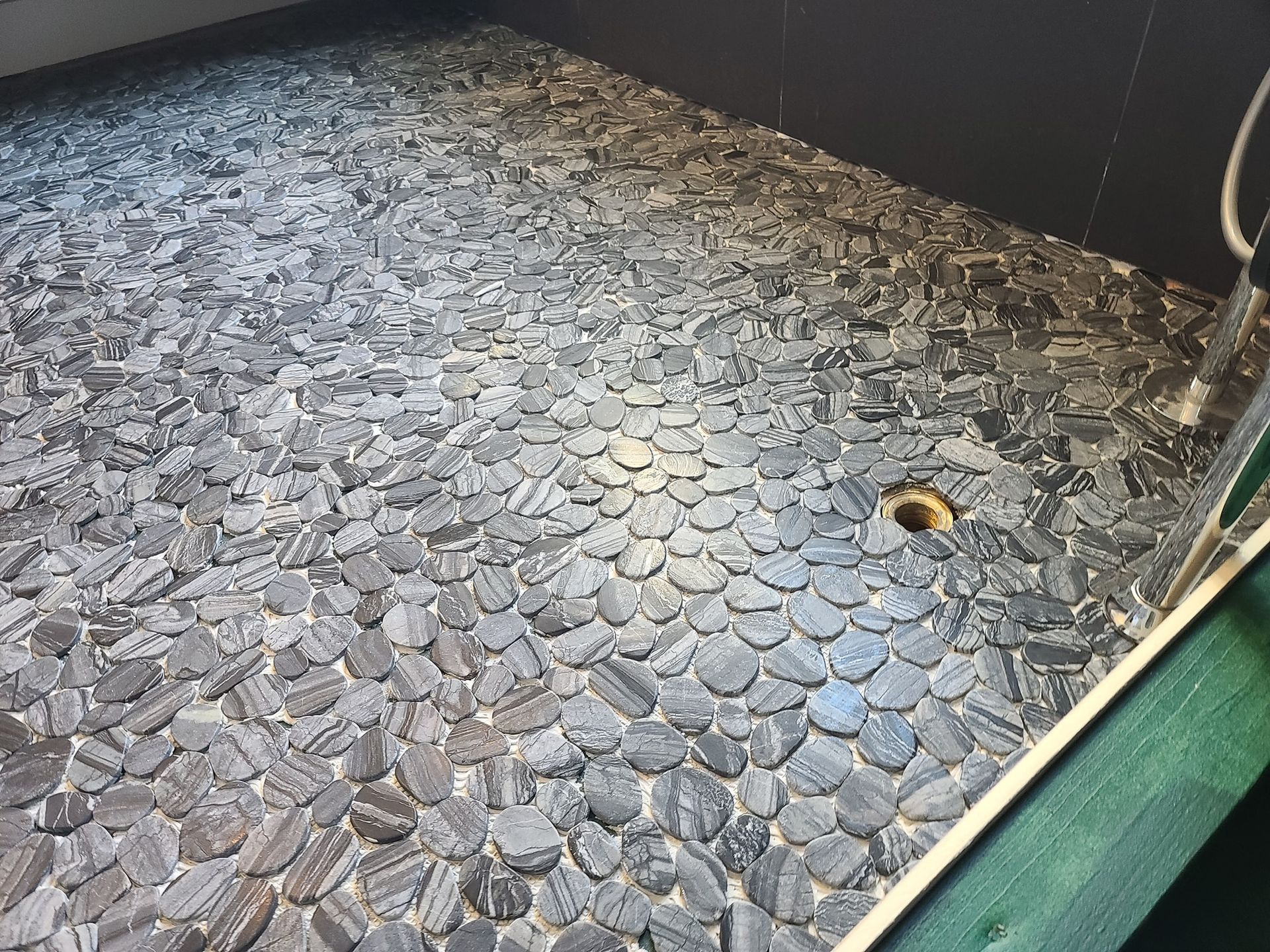 Shower floor covered in dark gray river stones, with a drain and a white pipe.