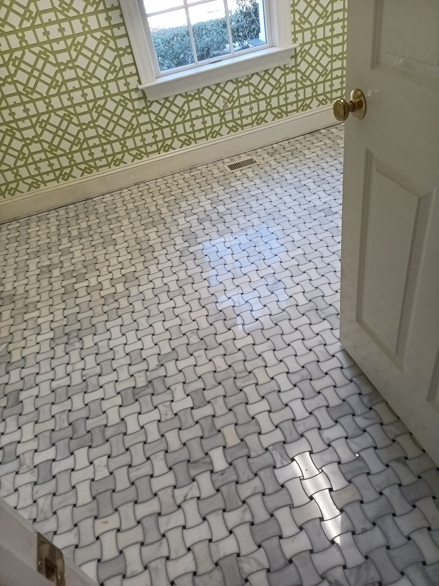 Bathroom with basketweave tile floor, green patterned wallpaper, and open white door.