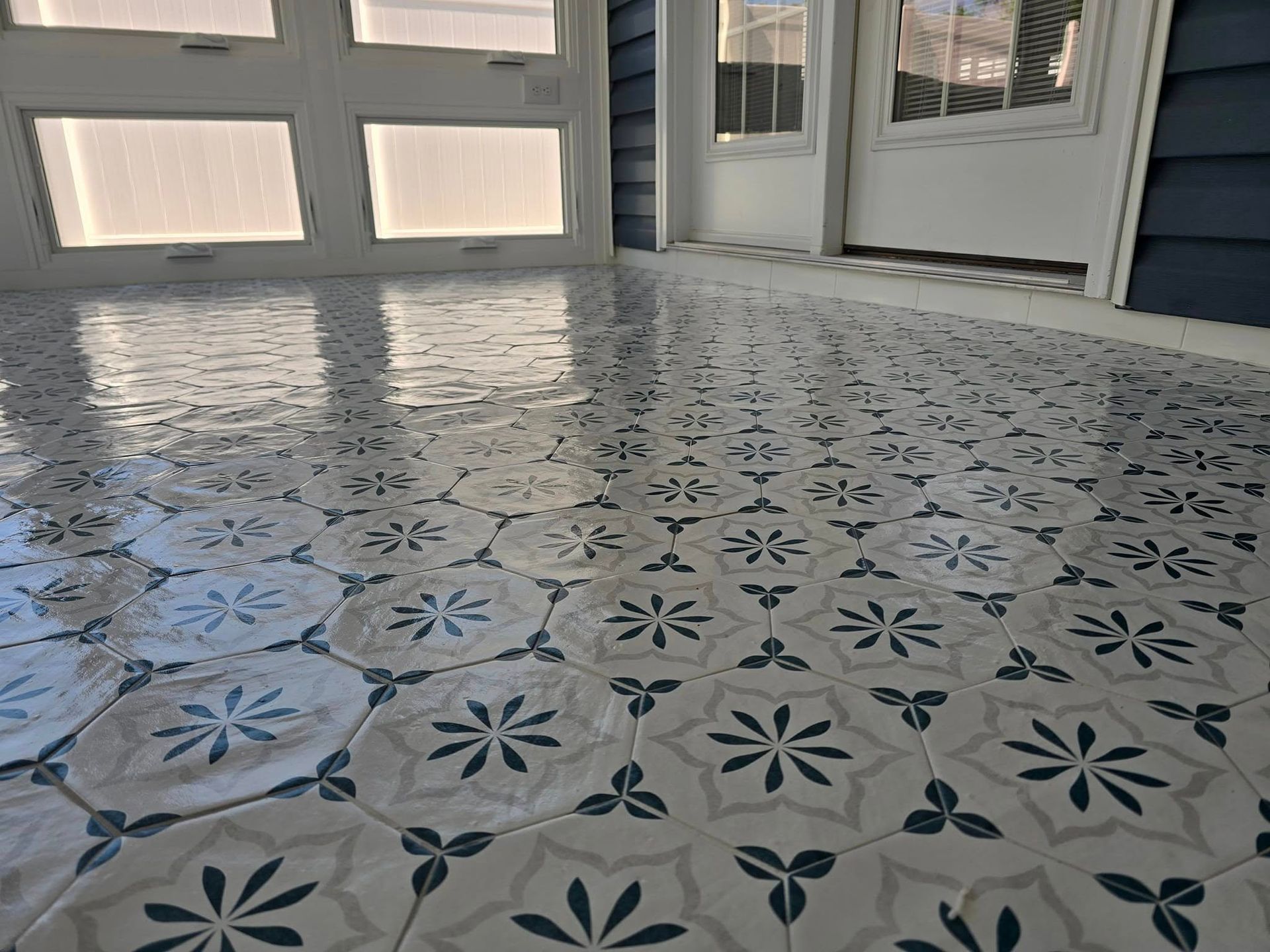 Patterned tile floor with white, gray, and blue floral designs; room with windows and door.
