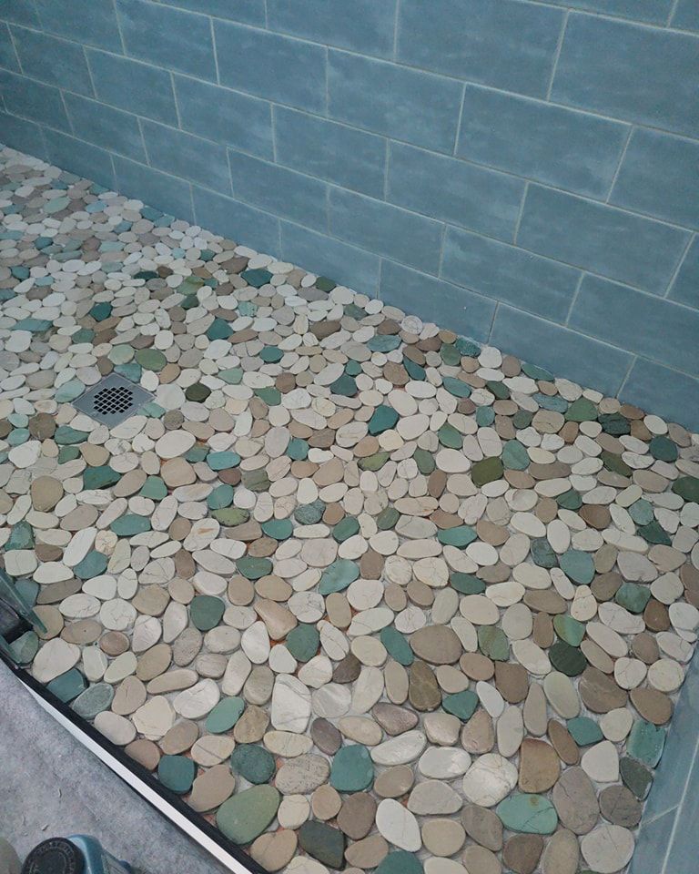 Shower with pebble-stone flooring and blue-green tiled walls.