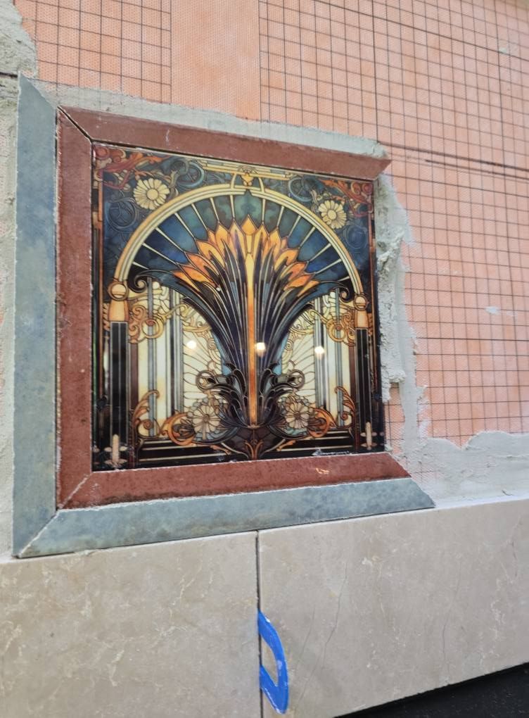 Decorative tile with a stylized, arch-shaped design framed in dark red, set into a wall.