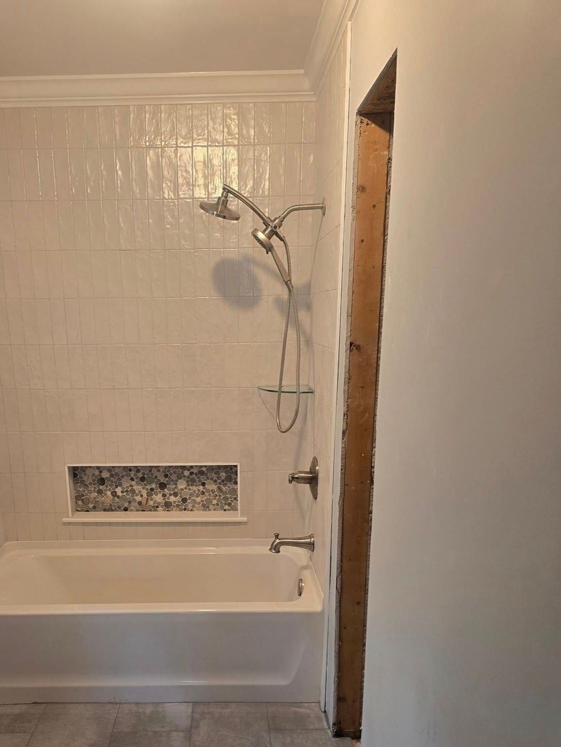 Bathroom with white tiled shower/tub, fixtures, and a partially open wall revealing wood.