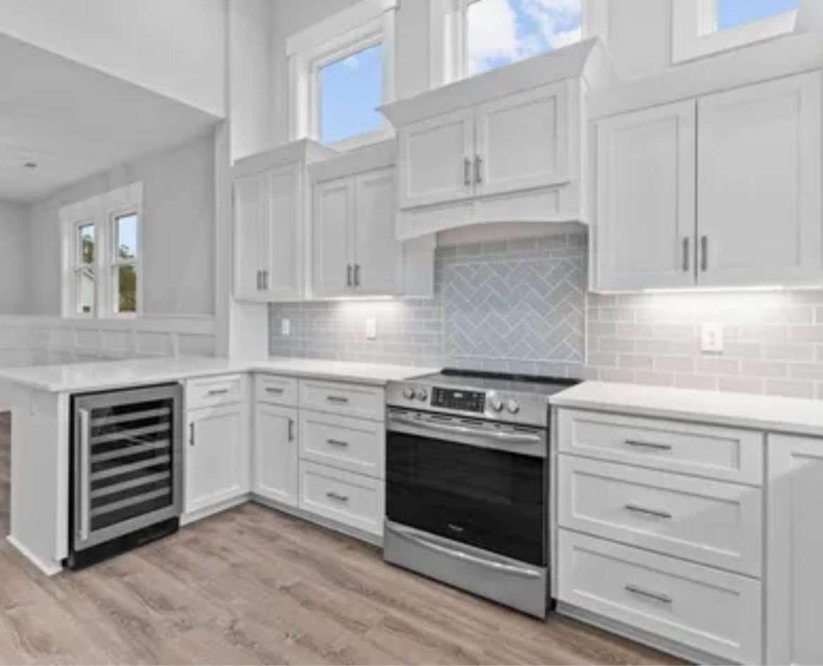 Bright modern kitchen with white cabinets, stainless stove, wine cooler, and light wood floors