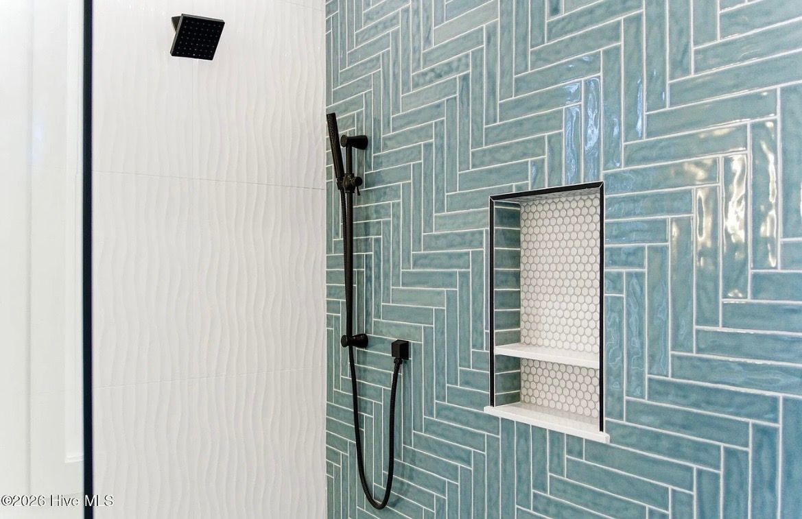 Blue herringbone tile shower with a square niche and black shower fixtures beside a white wall