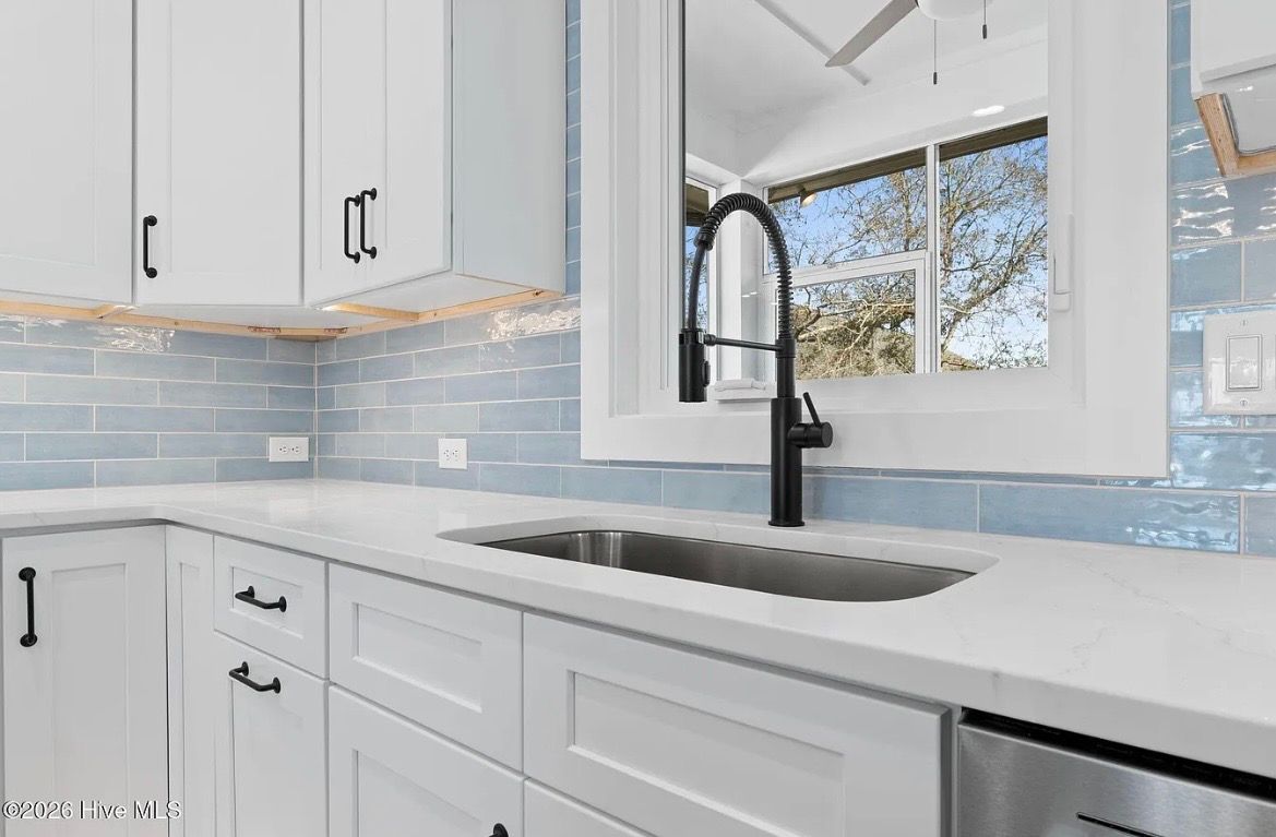 Bright white kitchen with blue tile backsplash, black faucet, and window over a sink.