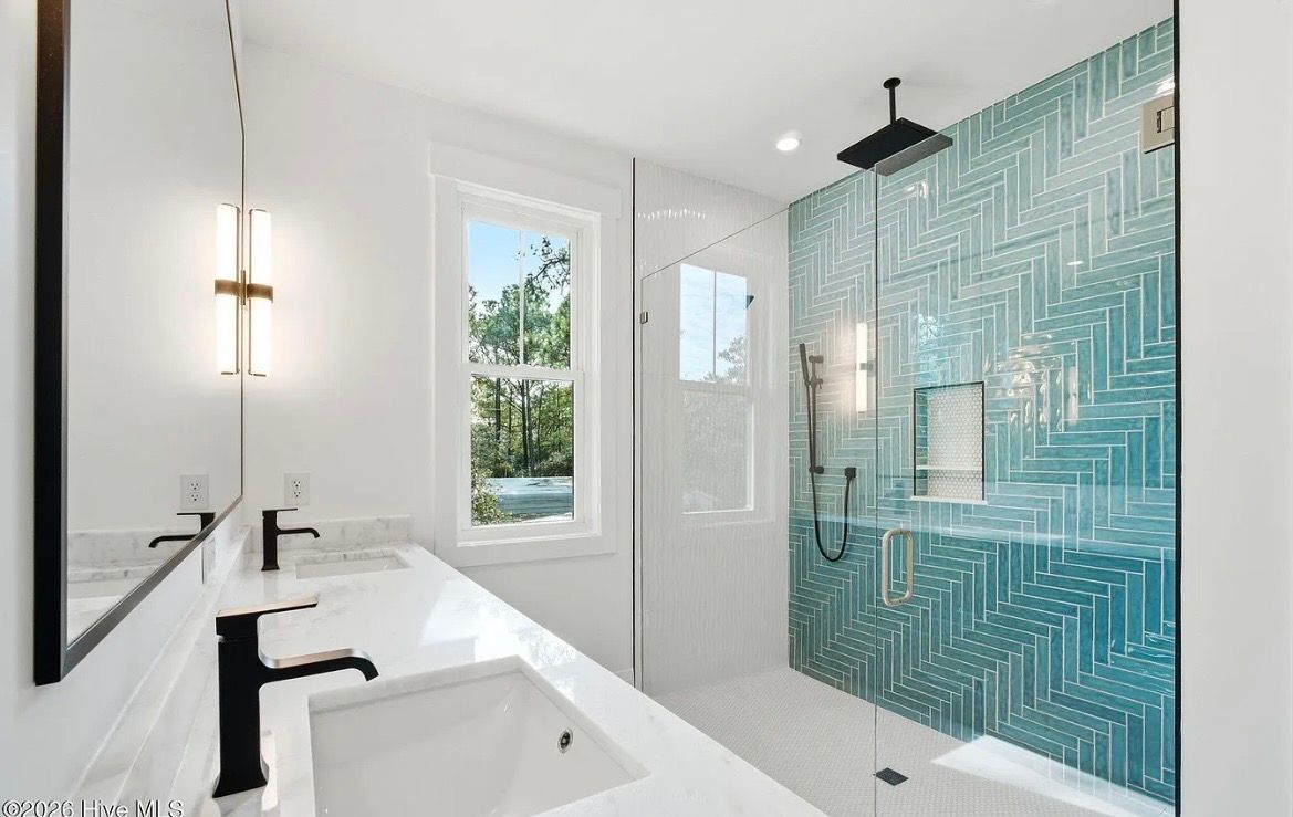 Modern bathroom with white vanity, black fixtures, and a glass shower with teal mosaic tile.