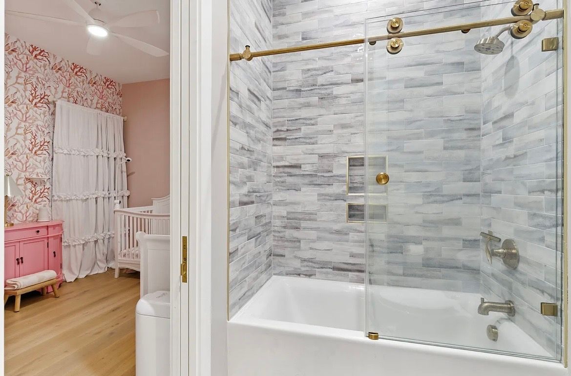 Bathroom doorway beside pink bedroom with white bed and gray marble tub surround