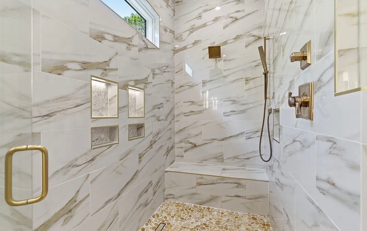Luxurious marble shower with gold fixtures, glass door, wall niches, and pebble floor