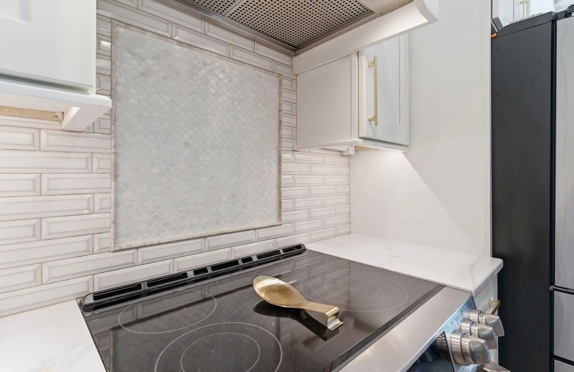 Modern white kitchen with black stovetop and stainless countertop, seen from the corner.