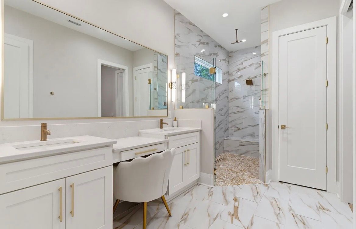 Bright white bathroom with marble tile, double vanity, large mirror, and glass-enclosed shower