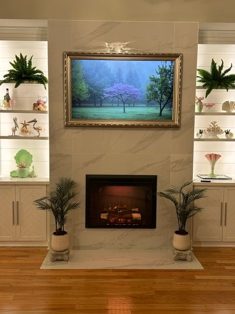 Elegant living room with a fireplace, framed landscape art, and white built-in shelves with decor objects.