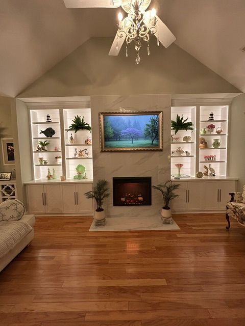 Living room with fireplace, built-in shelves, TV, chandelier, and hardwood floors