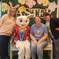 A group of women are posing for a picture with an easter bunny mascot.