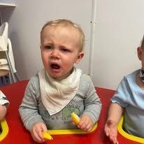 A baby is sitting at a table with a banana in his hand.