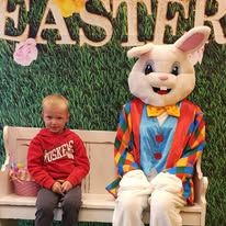 A little boy is sitting on a bench next to a bunny mascot.