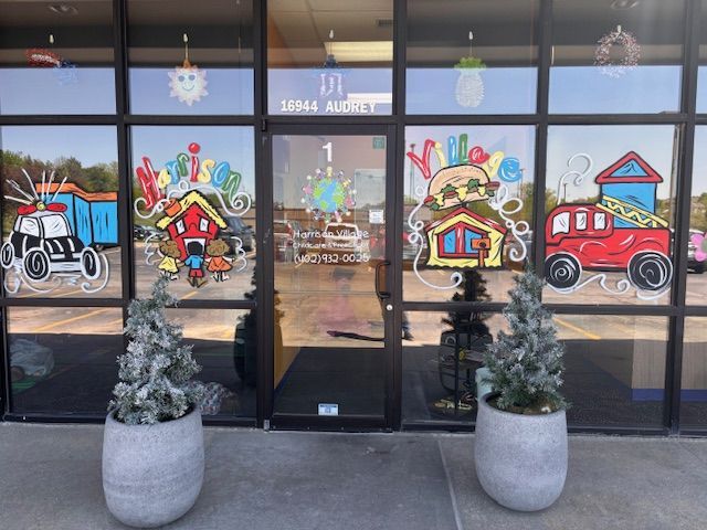 Two potted plants are in front of a building with drawings on the windows.