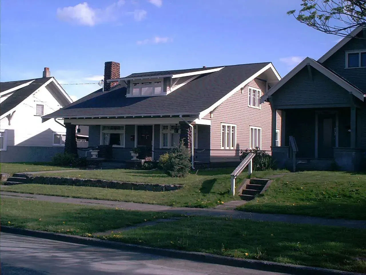 Suburban houses with front lawns on a sunny street, including a house with a porch and steps.