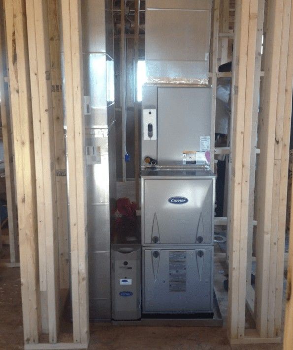 A metallic HVAC furnace unit installed within an unfinished wooden wall frame in a room under construction.