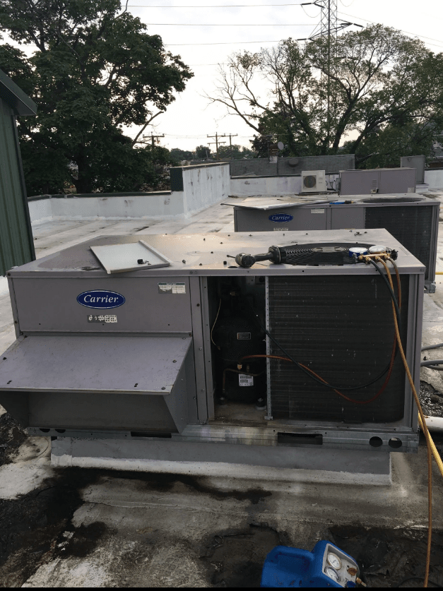 A grey Carrier rooftop air conditioning unit with an open side panel showing internal components on a flat roof.