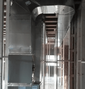 A vertical metal HVAC air duct system installed within the unfinished wooden framing of a building under construction.