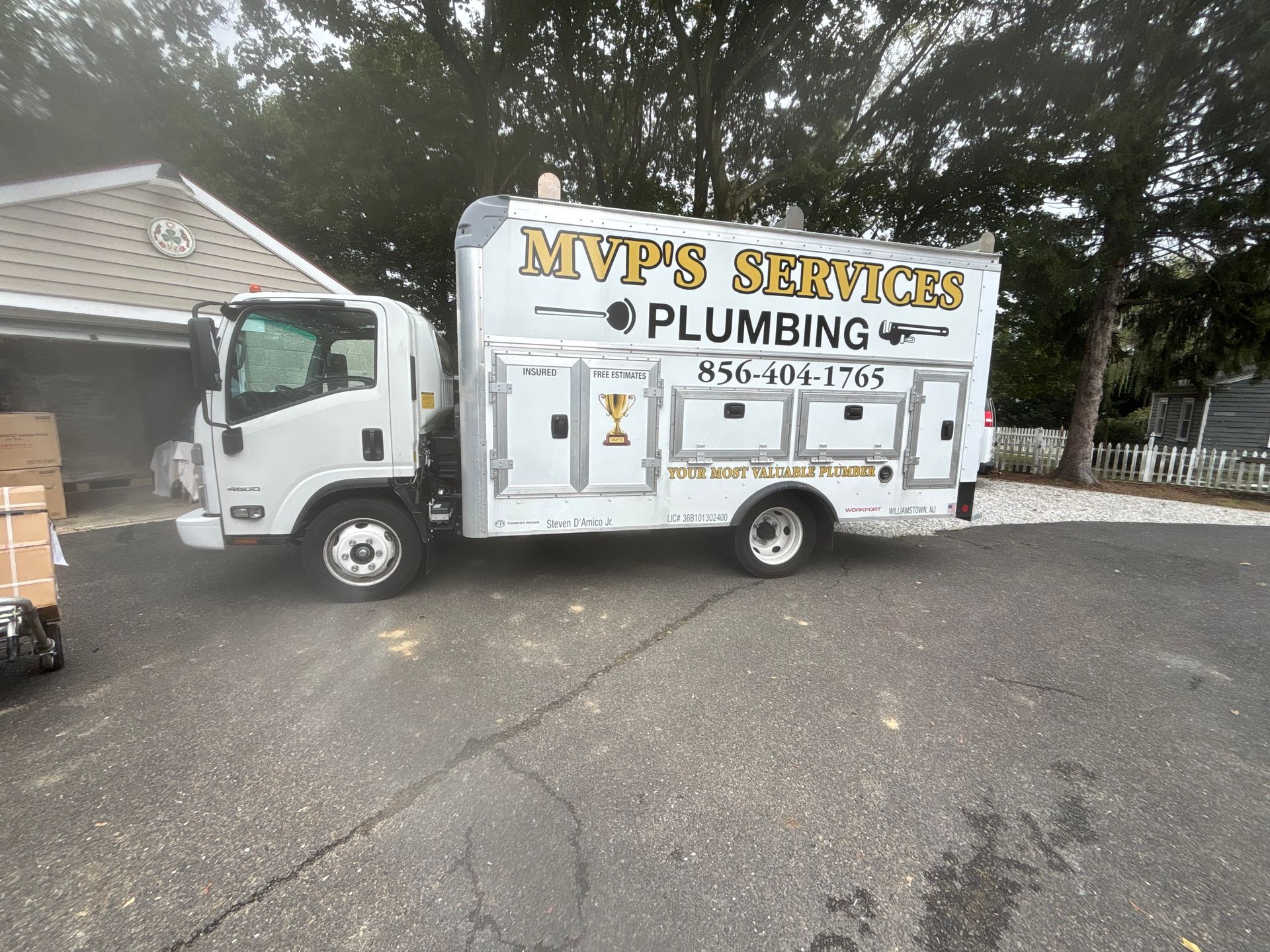 White MVP Service plumbing truck parked in a driveway beside a house and garage.