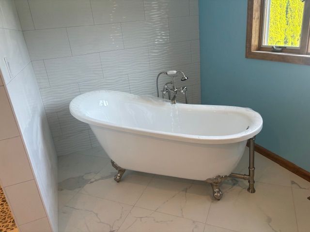 Clawfoot bathtub in a bathroom with white tile and blue walls, next to a shower with a window.