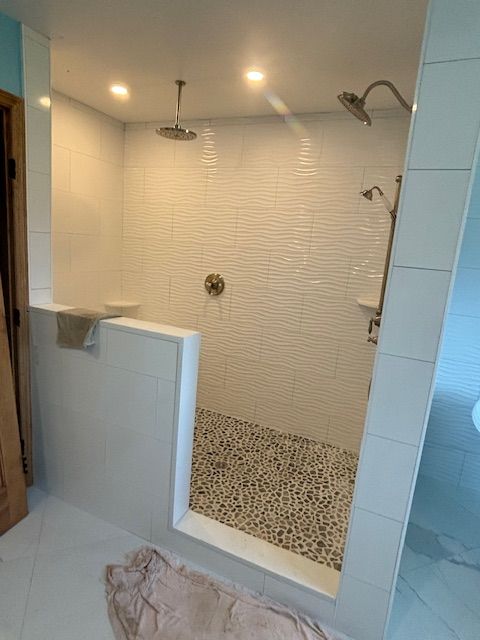Walk-in shower with white textured tile walls, pebble floor, and multiple shower heads.