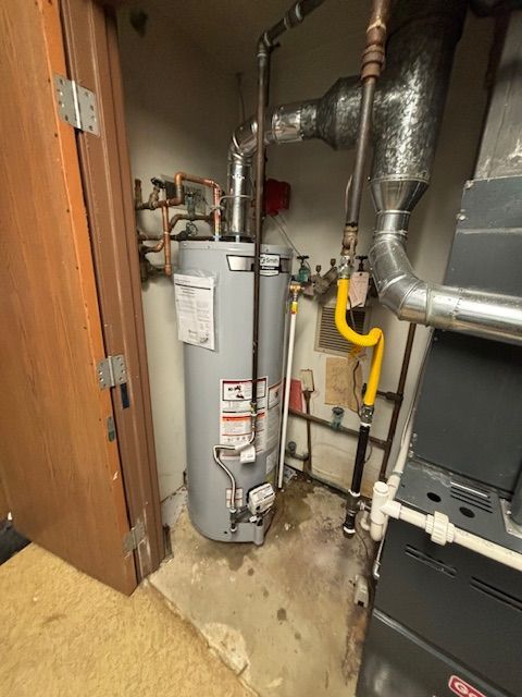 A water heater in a utility room next to a furnace and pipes. Gray and yellow components.