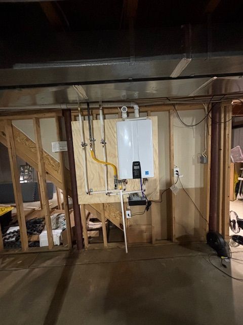 Tankless water heater mounted on a wooden wall in a basement. Gas and water pipes visible.