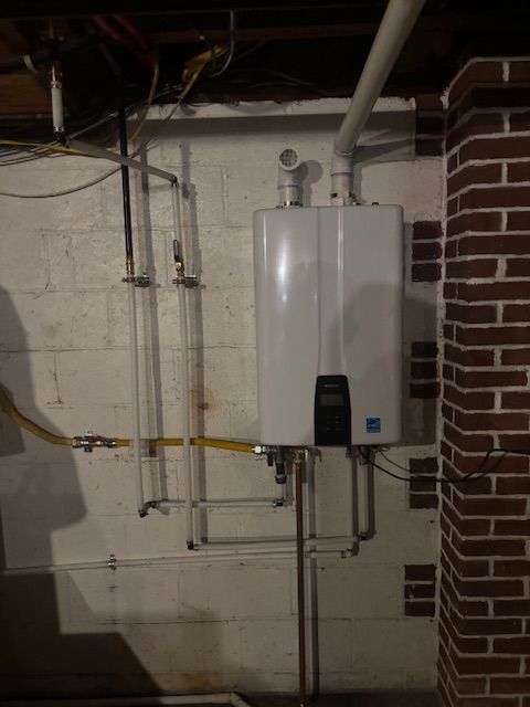 White tankless water heater installed in a basement, with copper and plastic piping.