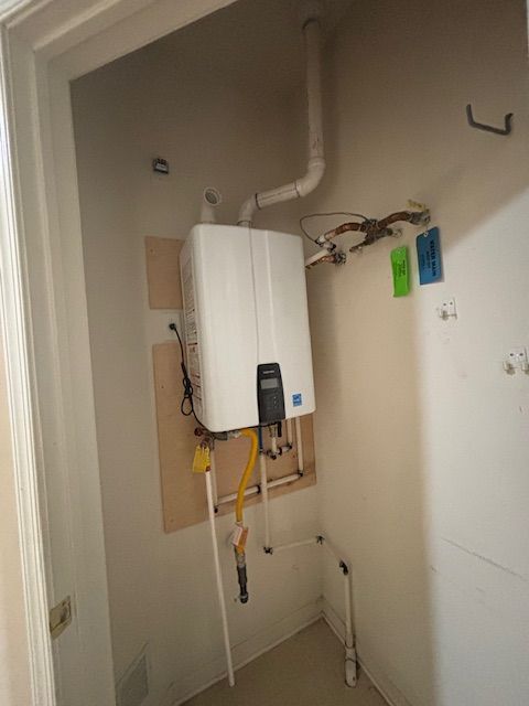 White tankless water heater installed in a small utility closet with gas and water lines.