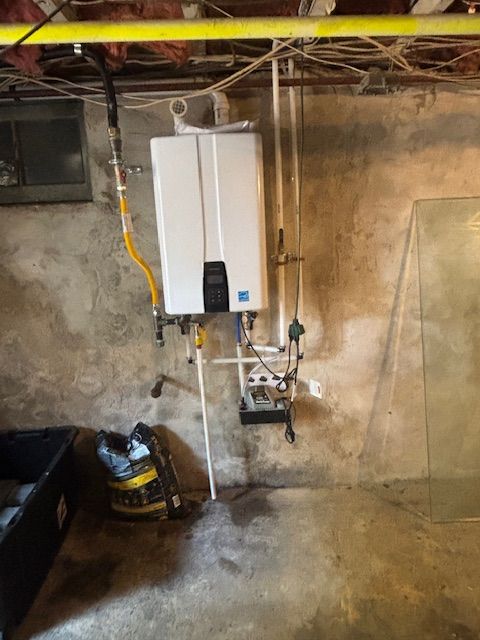 A tankless water heater mounted on a concrete wall in a basement.