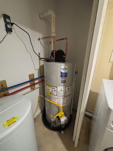 Water heater in a utility closet with associated pipes and electrical connections.