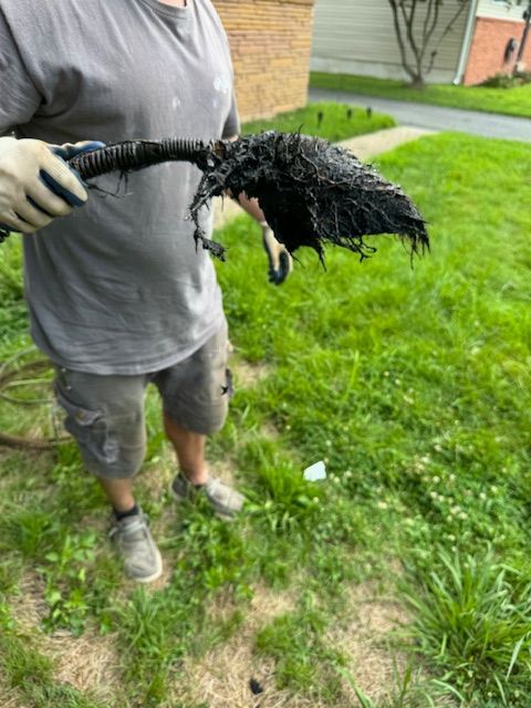 Person holding a clogged, black pipe with matted debris outside on grass.