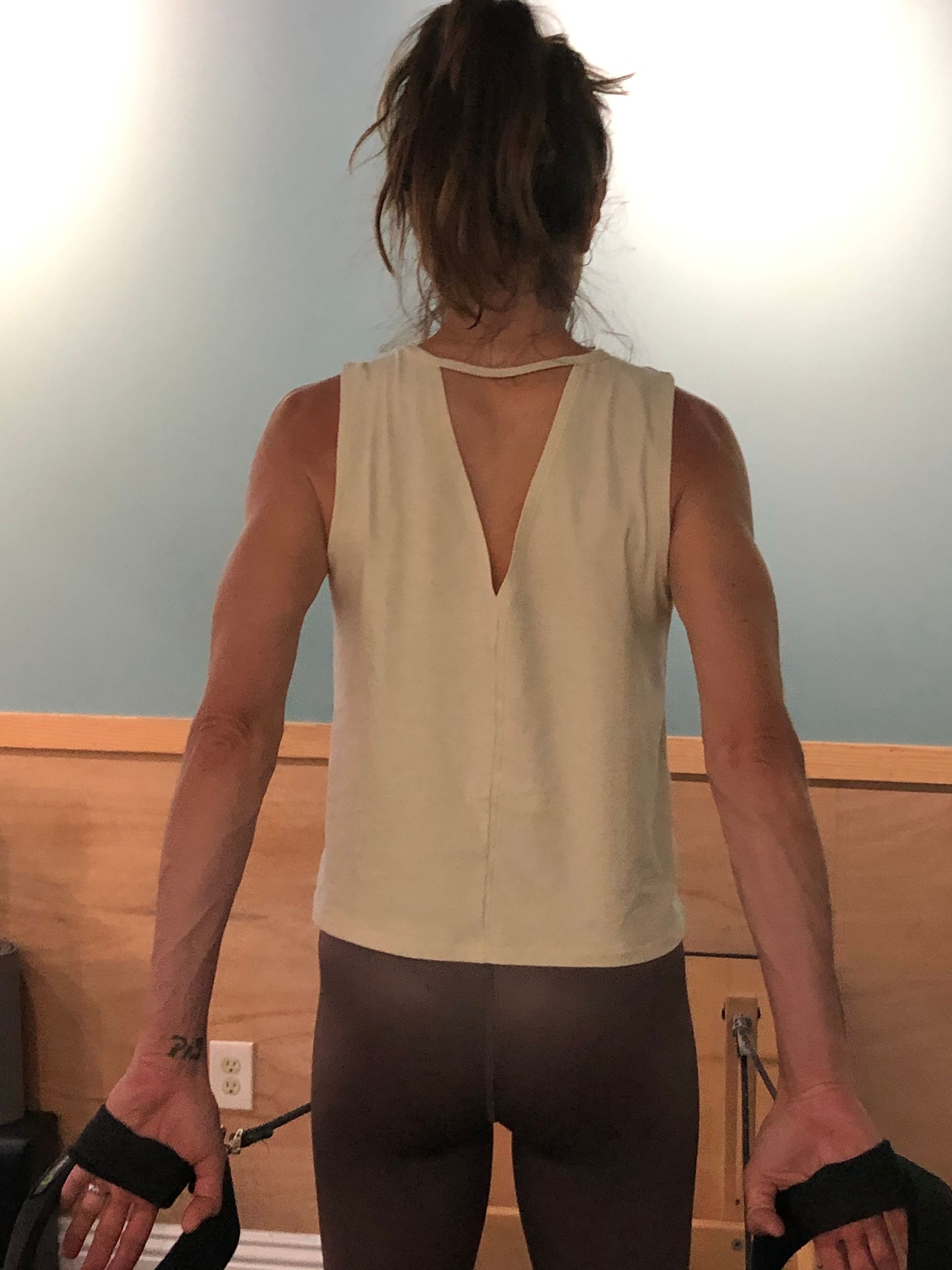 The back of a woman wearing a white tank top and brown pants