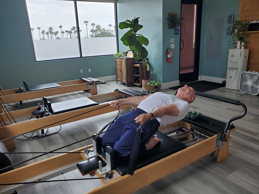 A man is laying on a pilates machine in a gym.