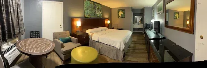 Room interior, featuring a bed, TV, dresser, table, chairs, artwork, and a neutral color scheme.