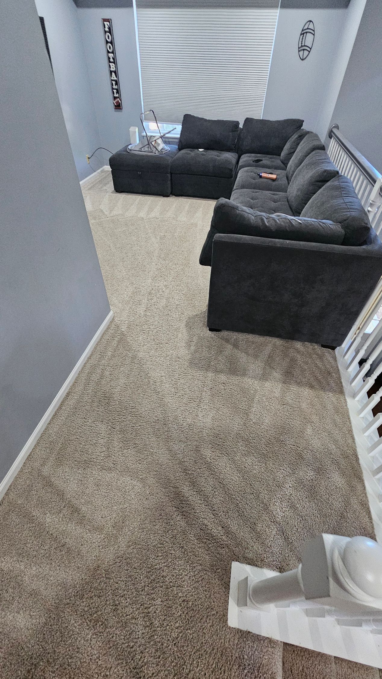 Carpeted living room with dark gray sectional sofa, doorway, and white shelving along the wall.
