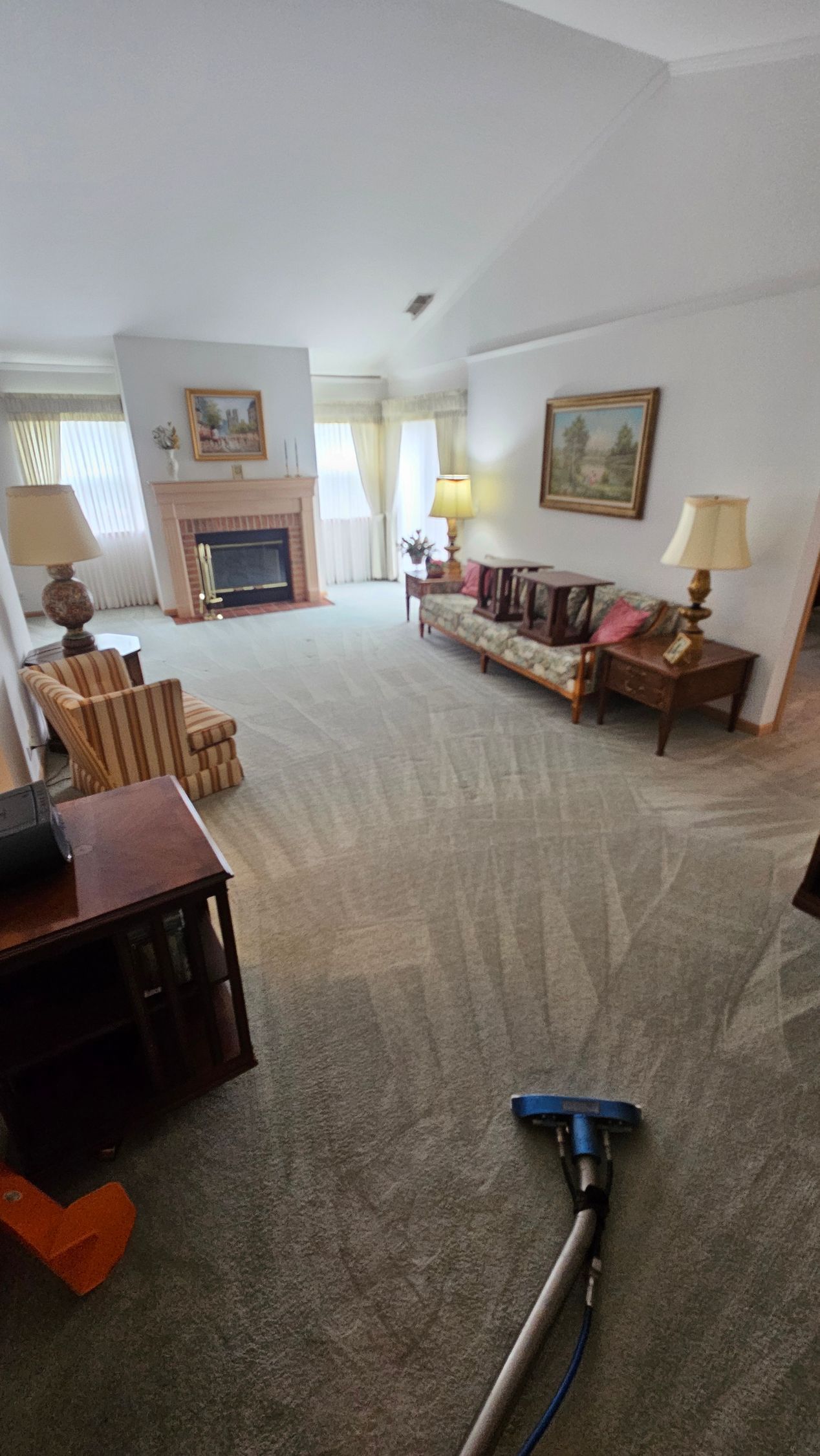 Bright living room with fireplace, sofa, lamp, and carpet cleaner on the floor