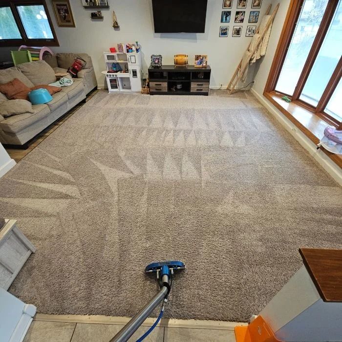 Living room with a carpet cleaner on a beige rug, couch, TV, and large windows.