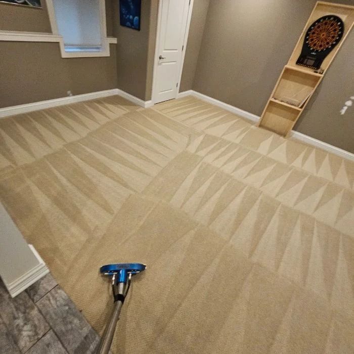 Carpet cleaner vacuuming a beige carpet in a finished basement room with a dartboard on the wall