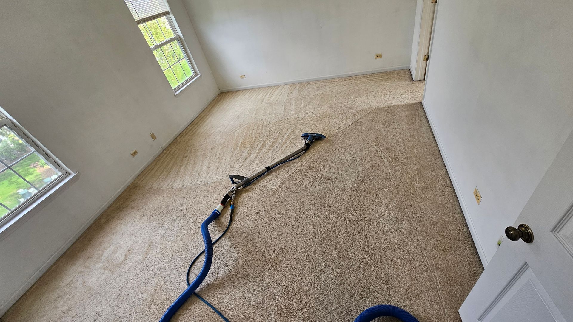 Empty carpeted room with a vacuum hose and bright windows on the left wall