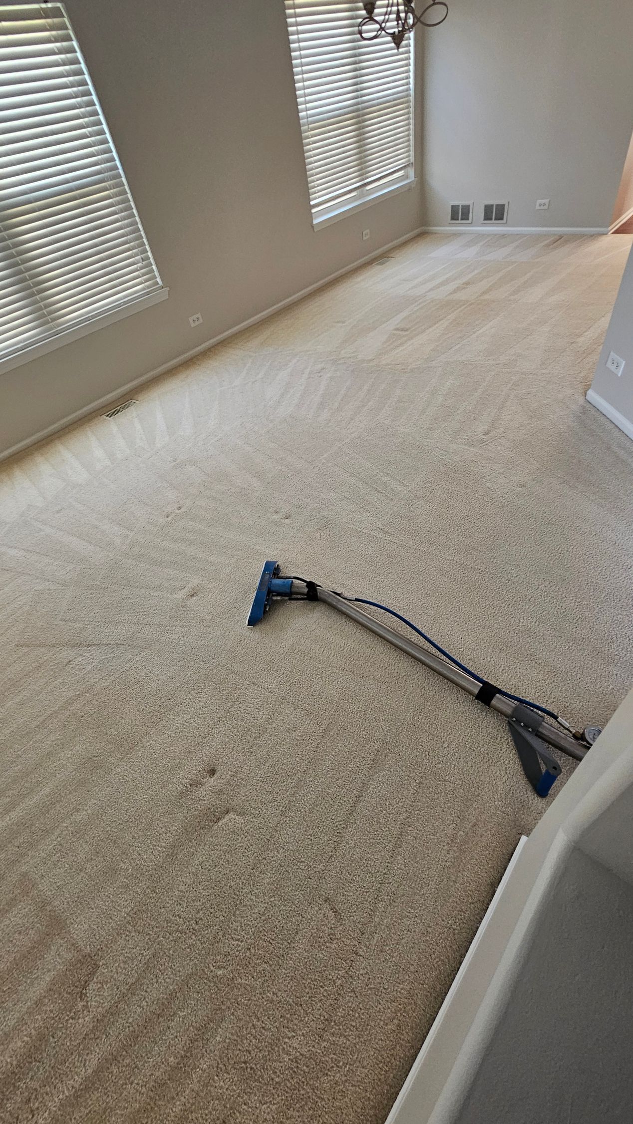 Carpeted room with a power tool on the floor near window blinds and wall outlets