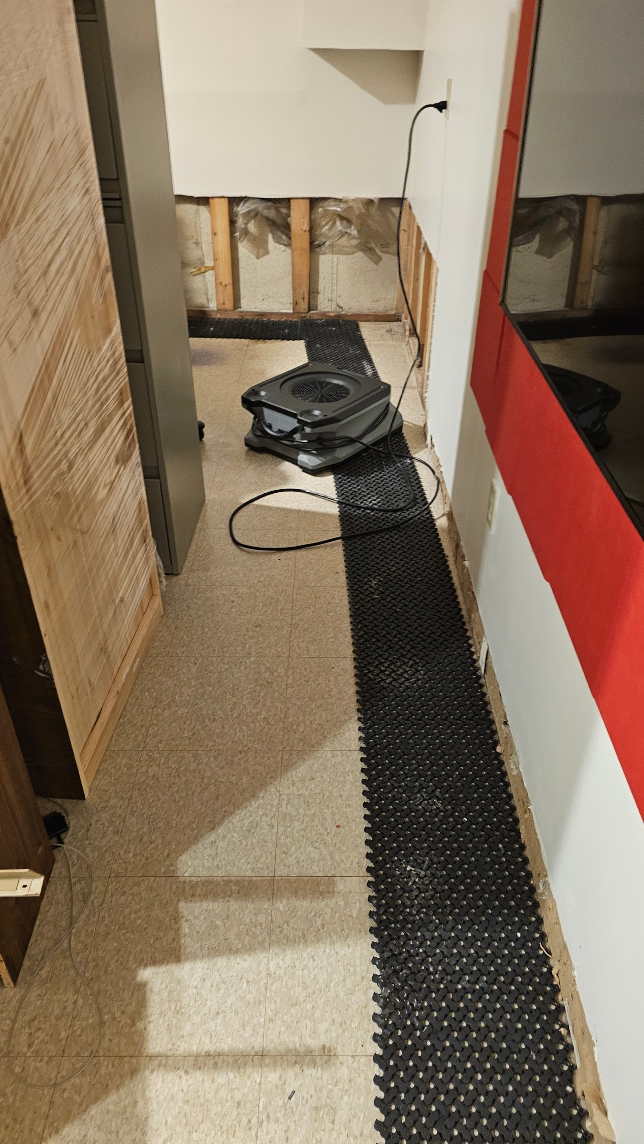 Narrow hallway with construction debris and a black runner beside a red-and-white wall