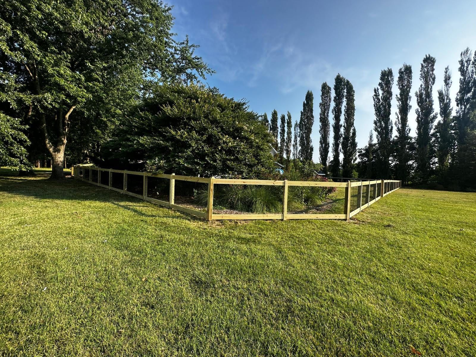 A wooden fence surrounds a grassy field with trees in the background.