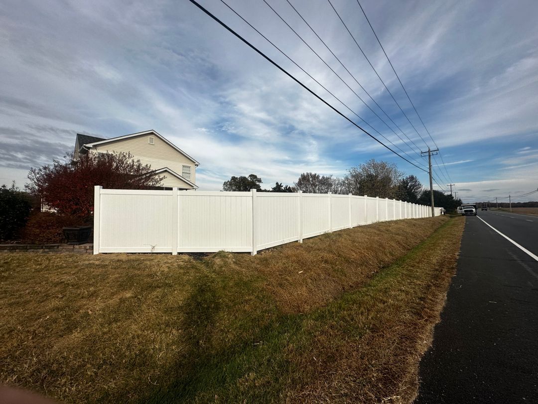 A white fence is along the side of a road next to a house.