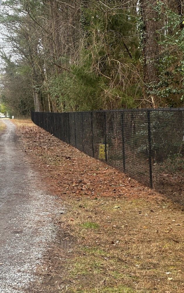 A chain link fence along a dirt road in the woods.