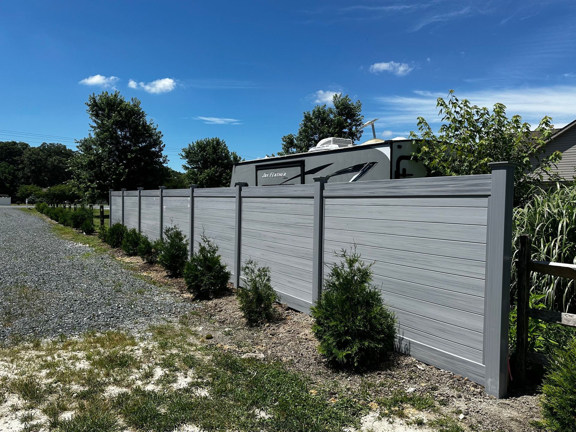 A gray fence surrounds a gravel driveway in front of a house.