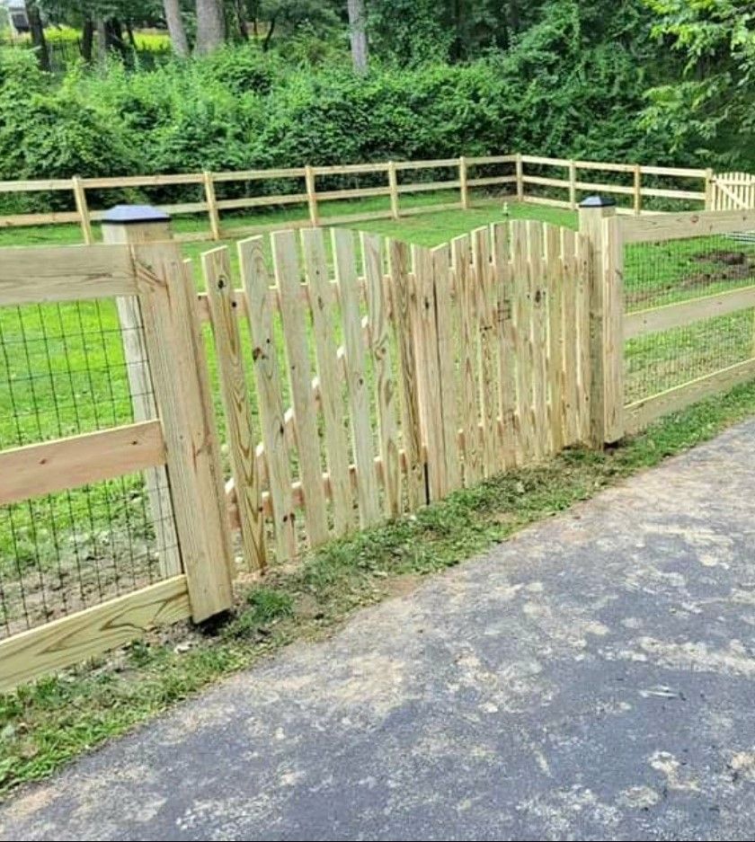 A wooden fence with a gate in the middle of a driveway.