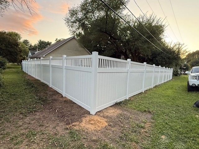 White vinyl fence surrounding a yard, with a house and trees in the background.